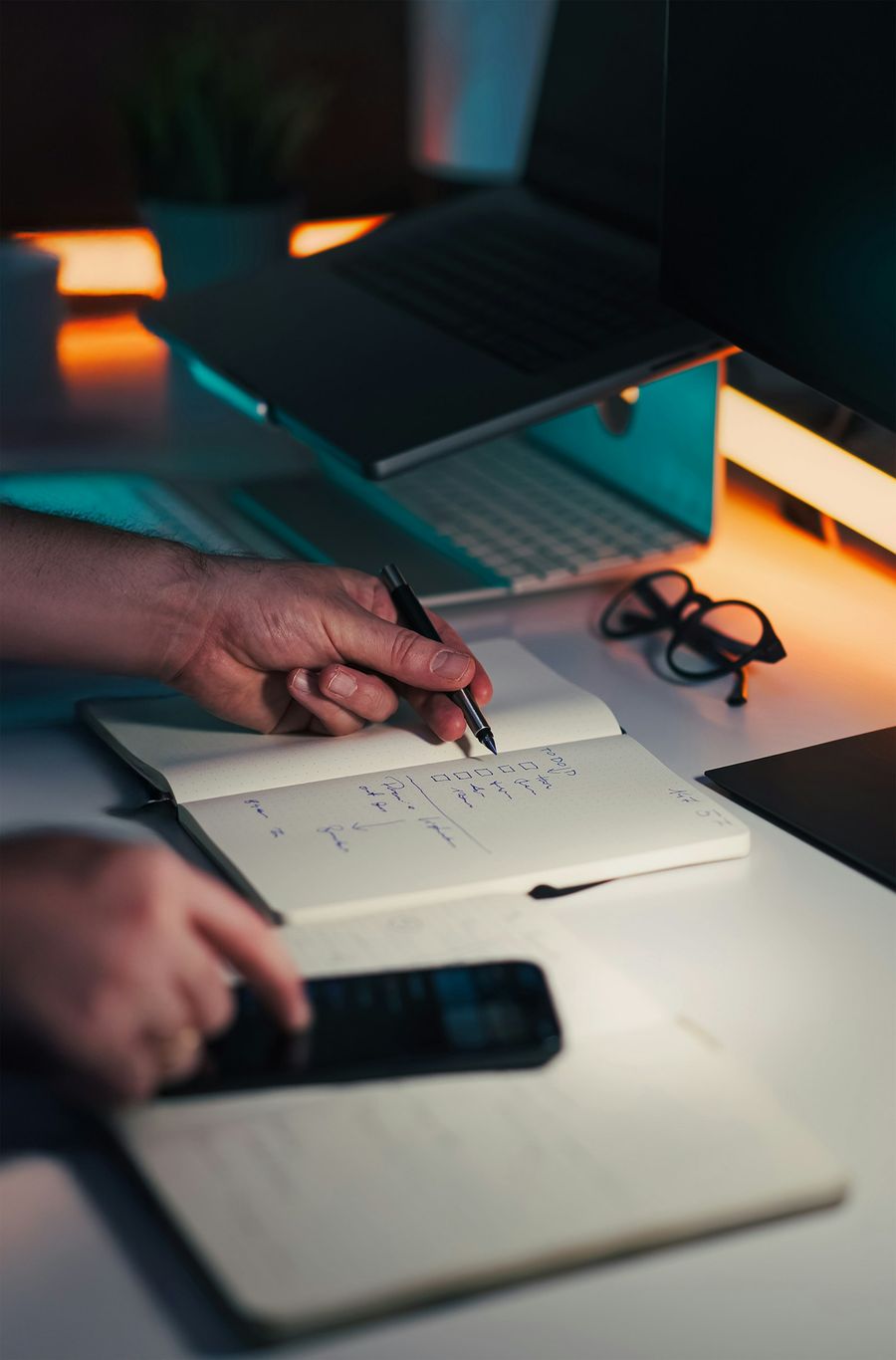 Hands planning in a notebook beside a laptop and phone